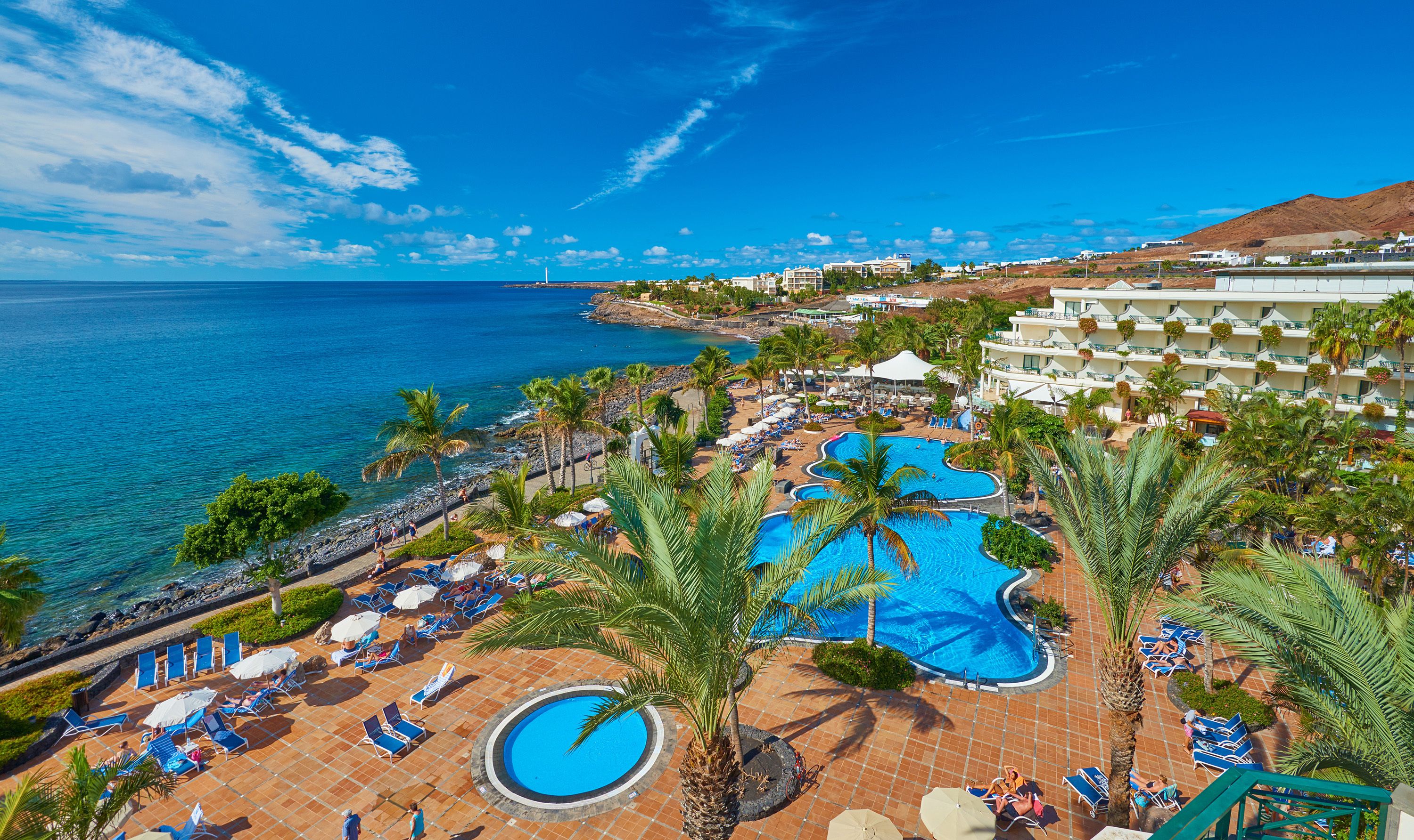 Un resort con una piscina grande, palmeras y vista al océano.