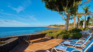 A beachside patio with lounge chairs, a stone wall, and a view of the ocean.