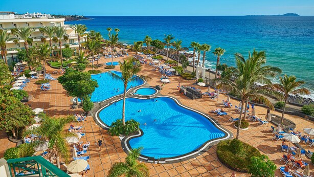 A resort with multiple swimming pools, palm trees, and a view of the ocean.