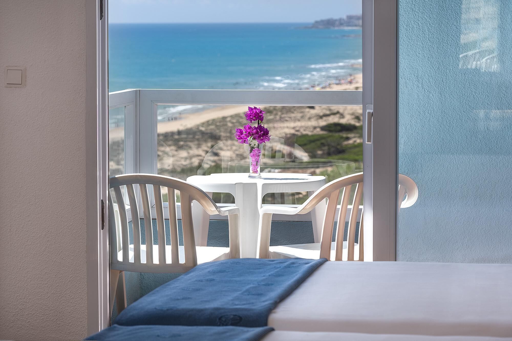 Ein Balkon mit Tisch und Stühlen mit Blick auf Strand und Meer.