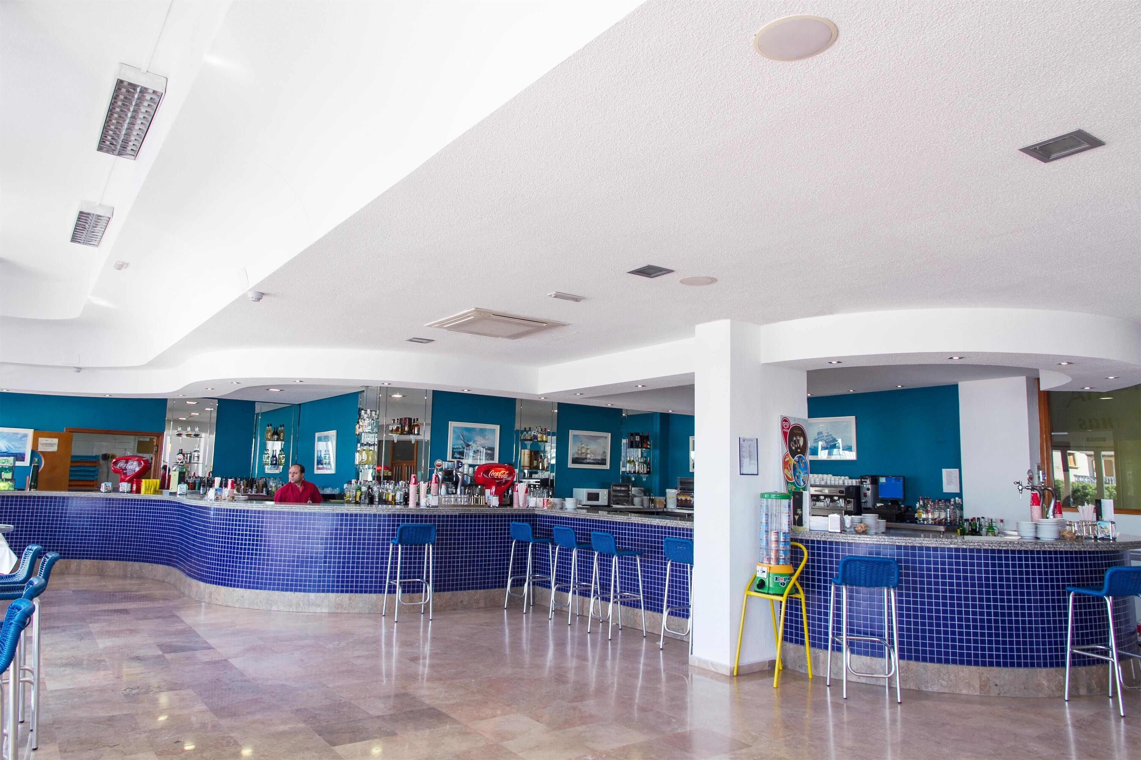 Een moderne barruimte met blauwe betegelde muren, diverse zitplaatsen en een bar met verschillende voorzieningen.