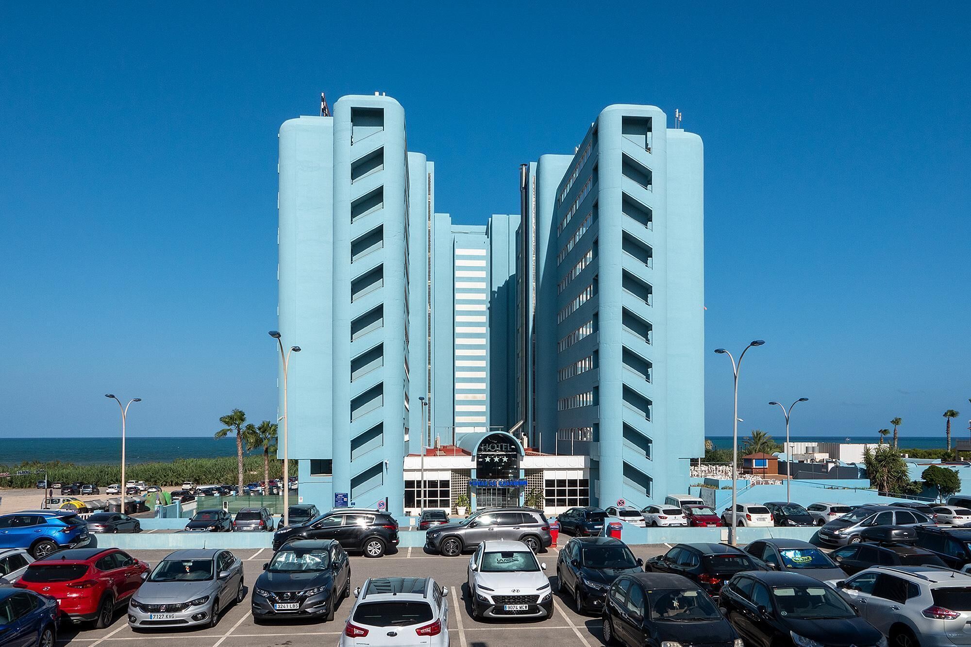 A hotel with a central entrance, multiple floors, and a parking lot filled with cars.