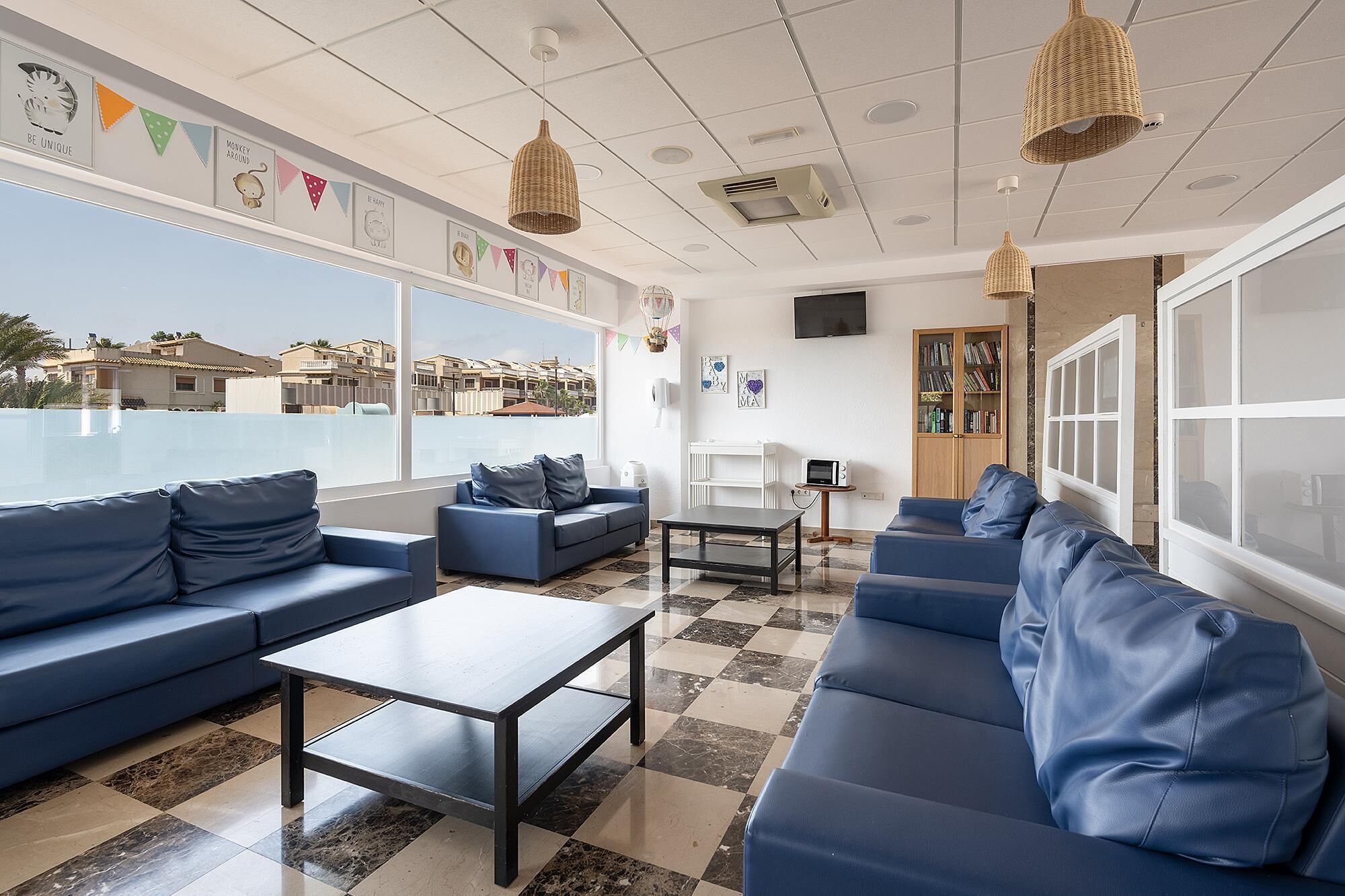 Ein moderner Loungebereich mit blauen Sofas, einem Couchtisch und Blick auf Gebäude durch große Fenster.