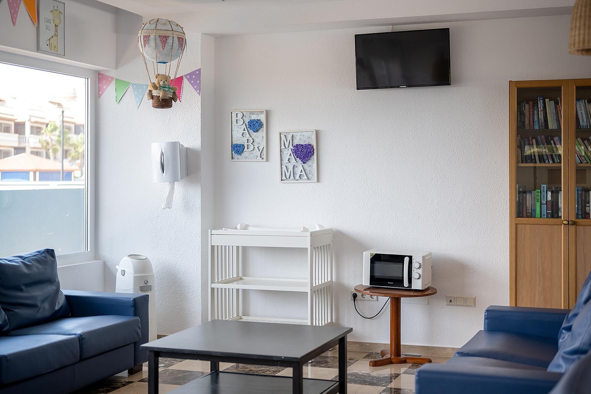 A living room with a white sofa, a blue sofa, a coffee table, a TV, a bookshelf, and a wall-mounted heater.