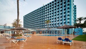 A large blue hotel with multiple balconies, a swimming pool, and sun loungers. - Hotel Playas de Guardamar (Guardamar del Segura)
