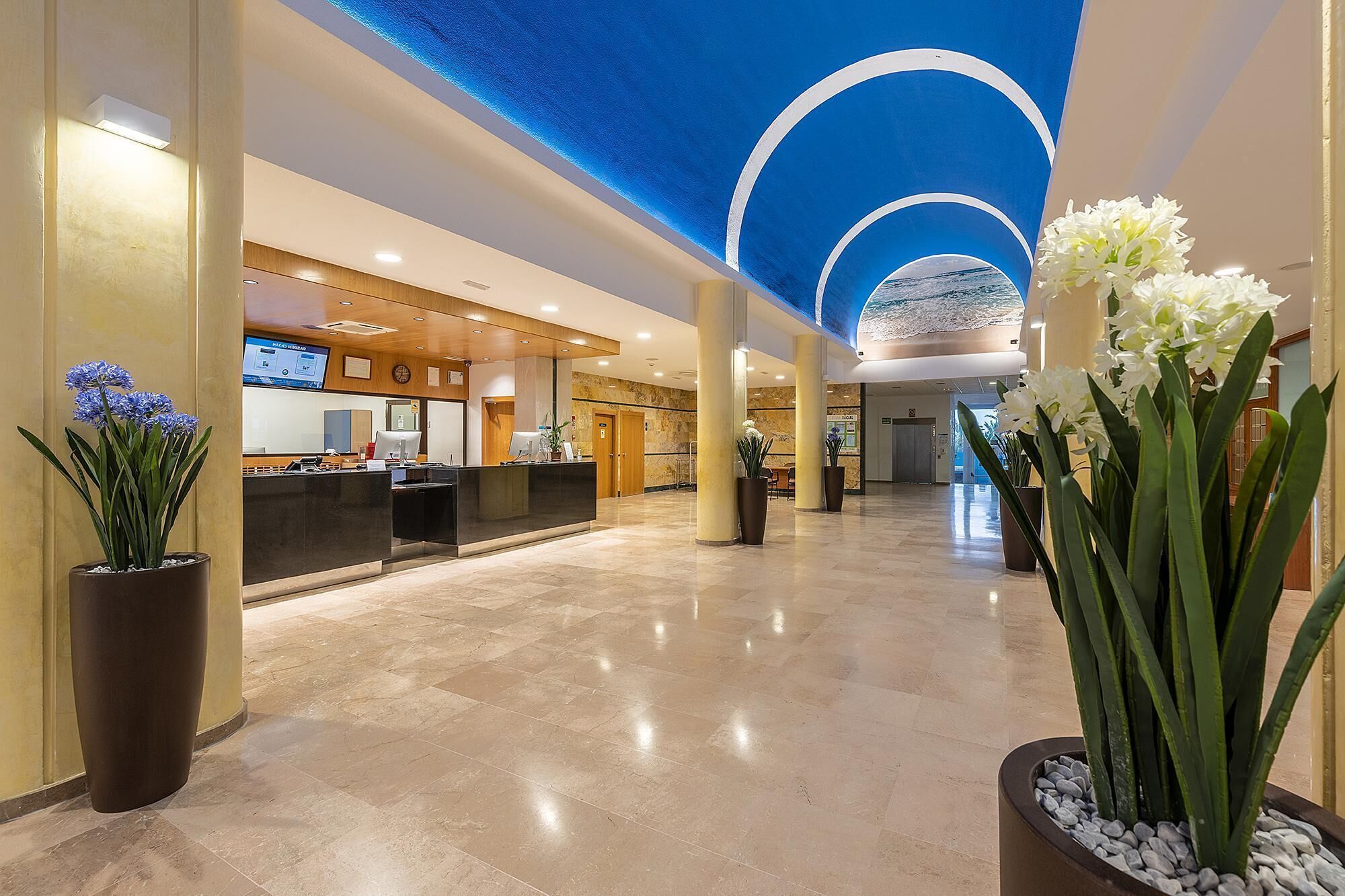 A hotel lobby with a reception desk, a digital screen, and a blue ceiling design.