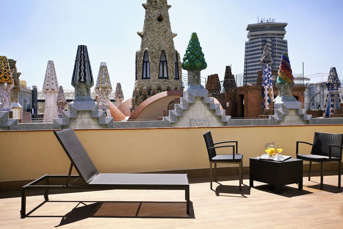 A rooftop terrace with lounge chairs, a small table with drinks, and a view of unique architectural structures.