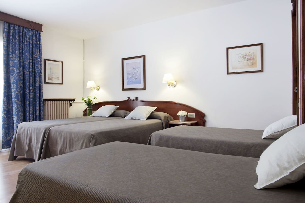A hotel room with two single beds, a wooden headboard, a nightstand with a lamp, and framed artwork on the walls.
