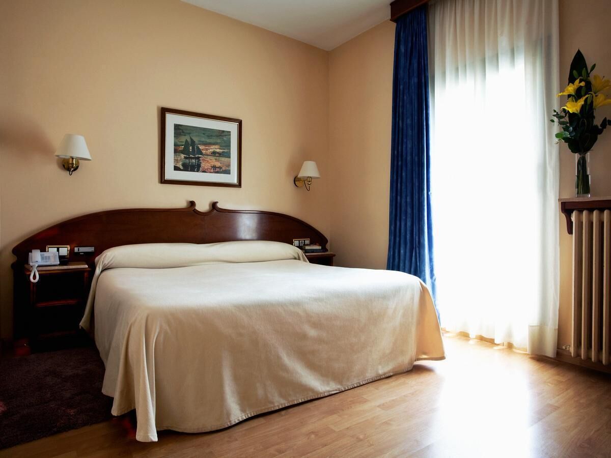 A hotel room with a bed, bedside tables, a lamp, a picture on the wall, and a window with curtains.