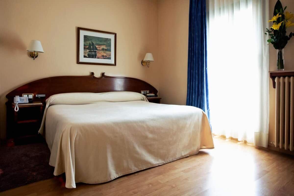 A hotel room with a bed, bedside tables, a lamp, a picture on the wall, and a window with curtains.