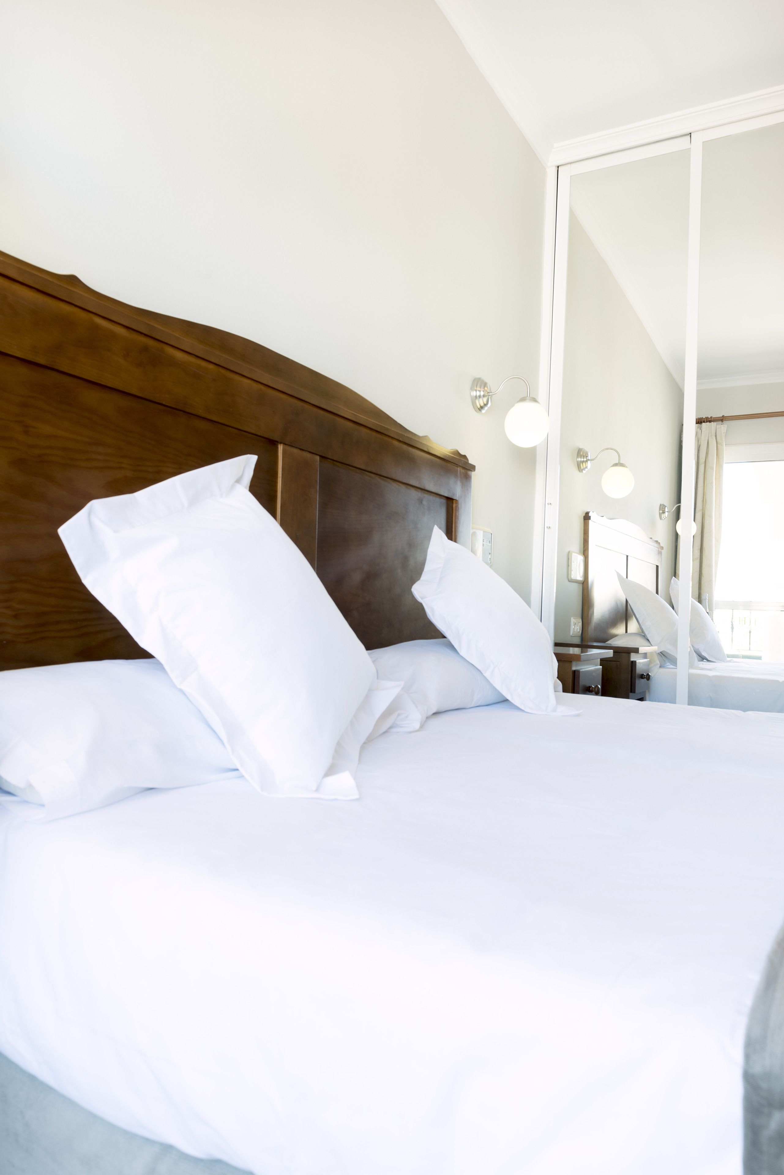 A neatly made bed with white linens and pillows, a wooden headboard, and a bedside table with a lamp.