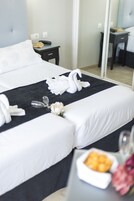 Une chambre d’hôtel avec un lit bien fait, une table de chevet avec un téléphone, un petit bol de fruits et un vase rempli de fleurs.