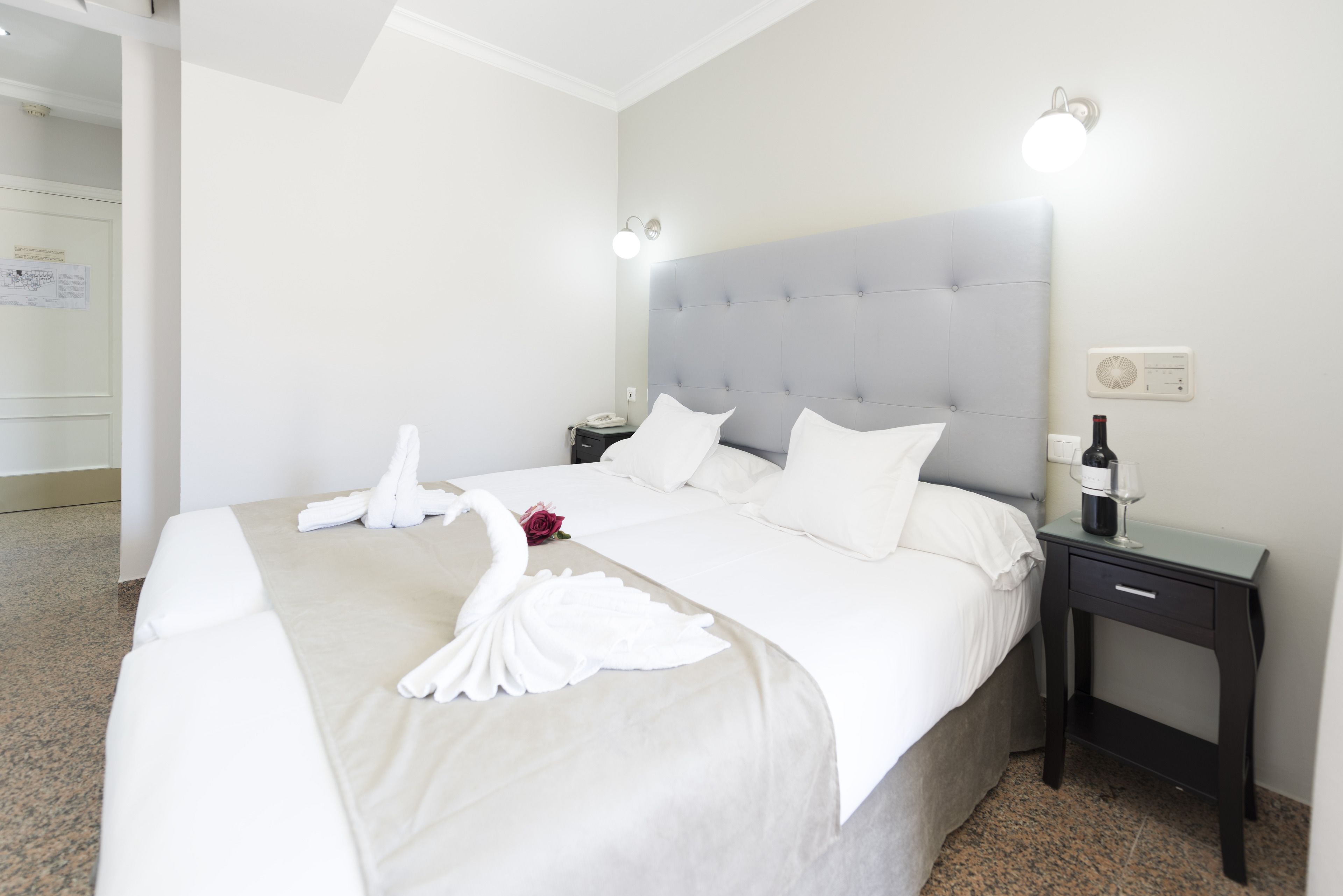 Una habitación de hotel con una cama grande, una mesita de noche y una lámpara de pared.