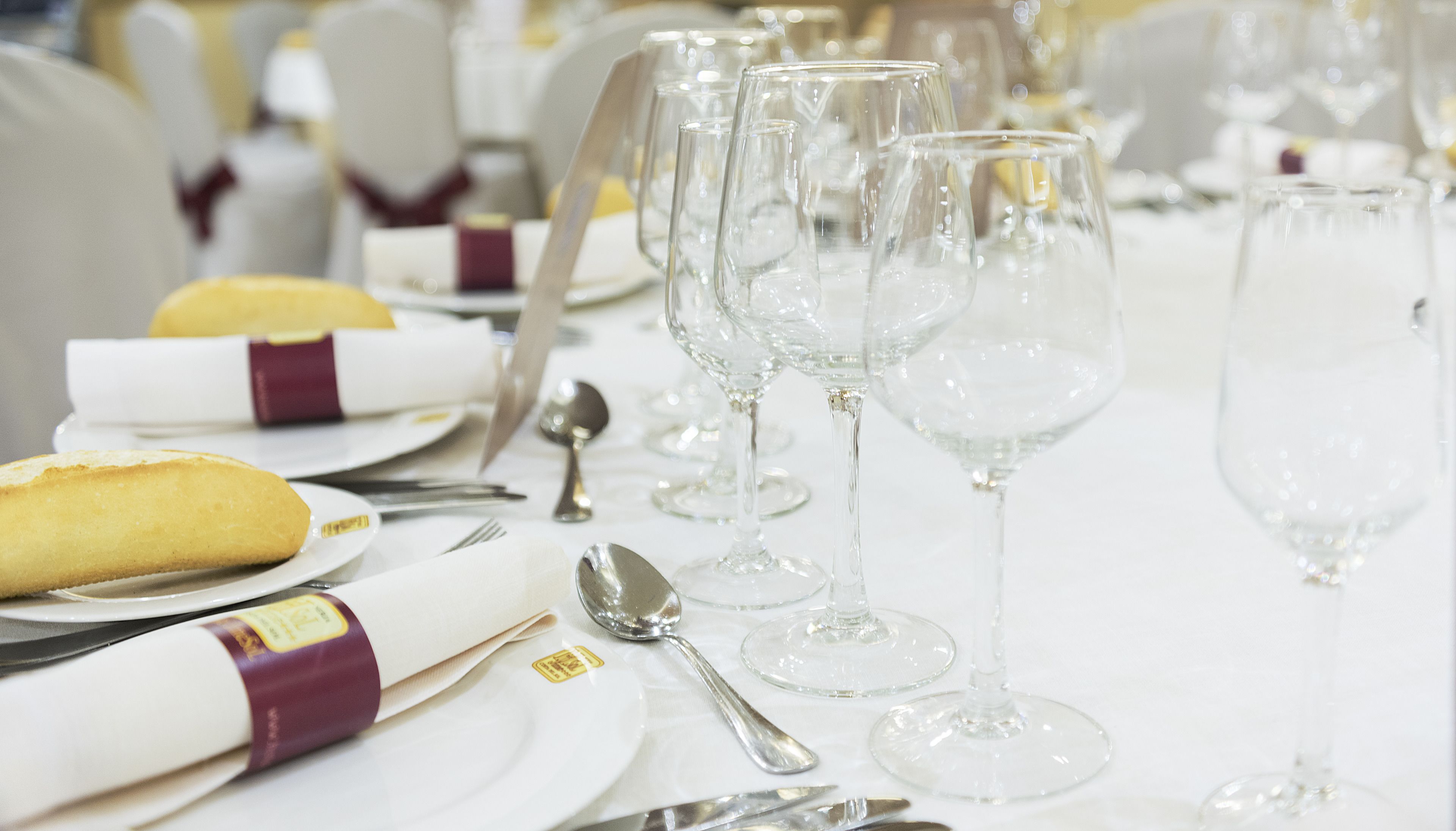 A table set for a formal event with clear glassware, folded napkins, and a bread roll.