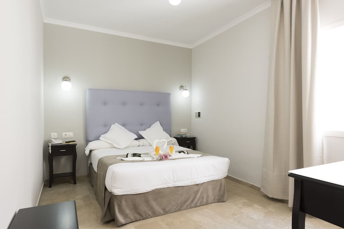Une chambre d’h ôtel bien rangée, avec un lit, des tables de chevet, une petite table et un rideau.