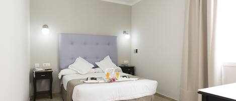Ein ordentlich eingerichtetes Hotelzimmer mit Bett, Nachttischen, einem kleinen Tisch und einem Vorhang.