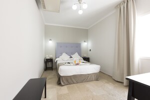 A hotel room with a bed, bedside tables, a bench, and a ceiling light fixture.