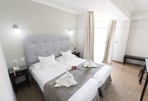 Et hotelværelse med en stor seng, et sengebord med en telefon, et skrivebord og en stol.