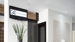 A reception desk with a wooden finish, a potted plant, and a sign above it. - Hotel Toboso Chaparil (Nerja)