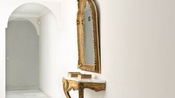 Een gang met een marmeren vloer, een witte muur en een spiegel met gouden lijst op een marmeren console.