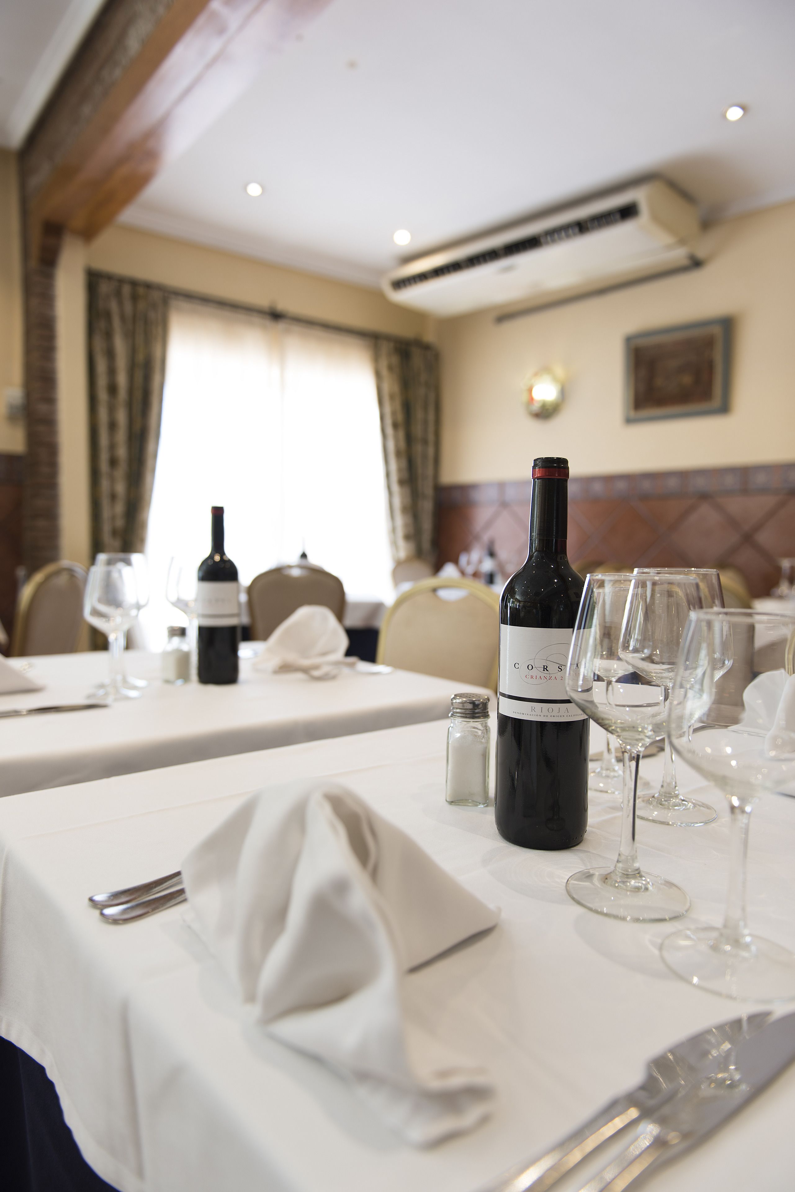 A dining table set with wine glasses, a bottle of wine, and cutlery.
