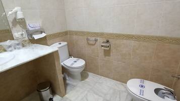 A bathroom with a white sink, a toilet, and a bidet. There is a trash bin and a towel rack.