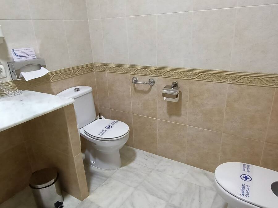 A bathroom with a white sink, a toilet, and a bidet. There is a trash bin and a towel rack.