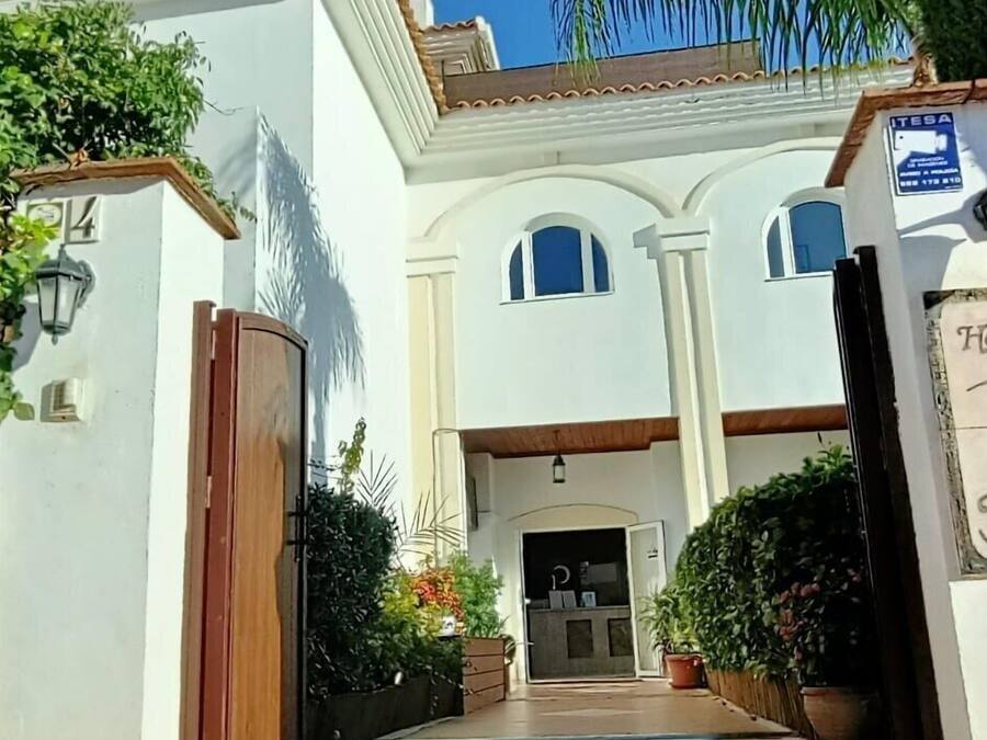 A two-story building with a white facade, a wooden gate, and a central entrance with a door.