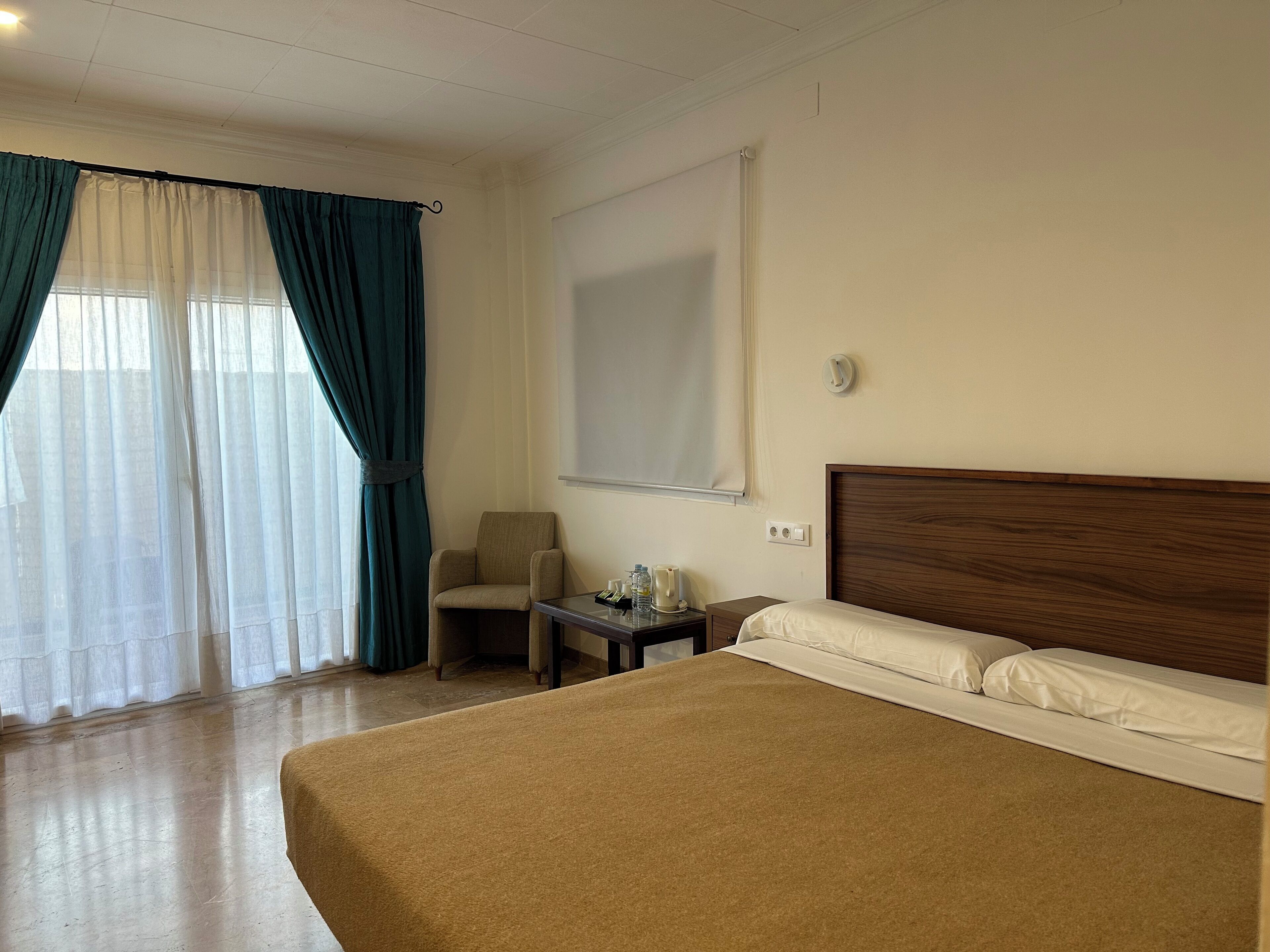 Una habitación de hotel con una cama grande, una silla, una mesita y una ventana con cortinas.