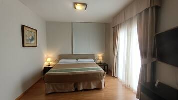 Una habitación de hotel con una cama grande, mesitas de noche con lámparas, un televisor de pantalla plana y un cuadro en la pared.