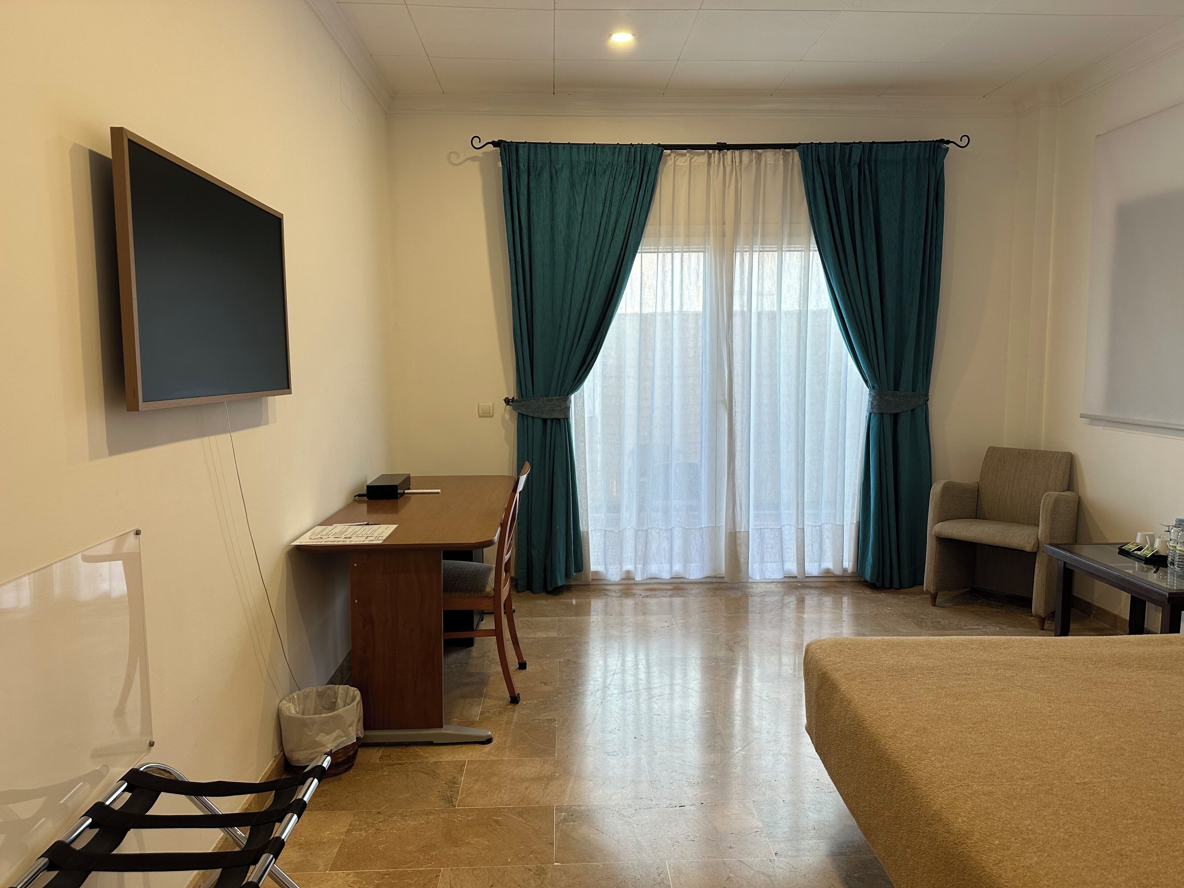Habitación de hotel con cama, escritorio, silla, televisor y ventana con cortinas.