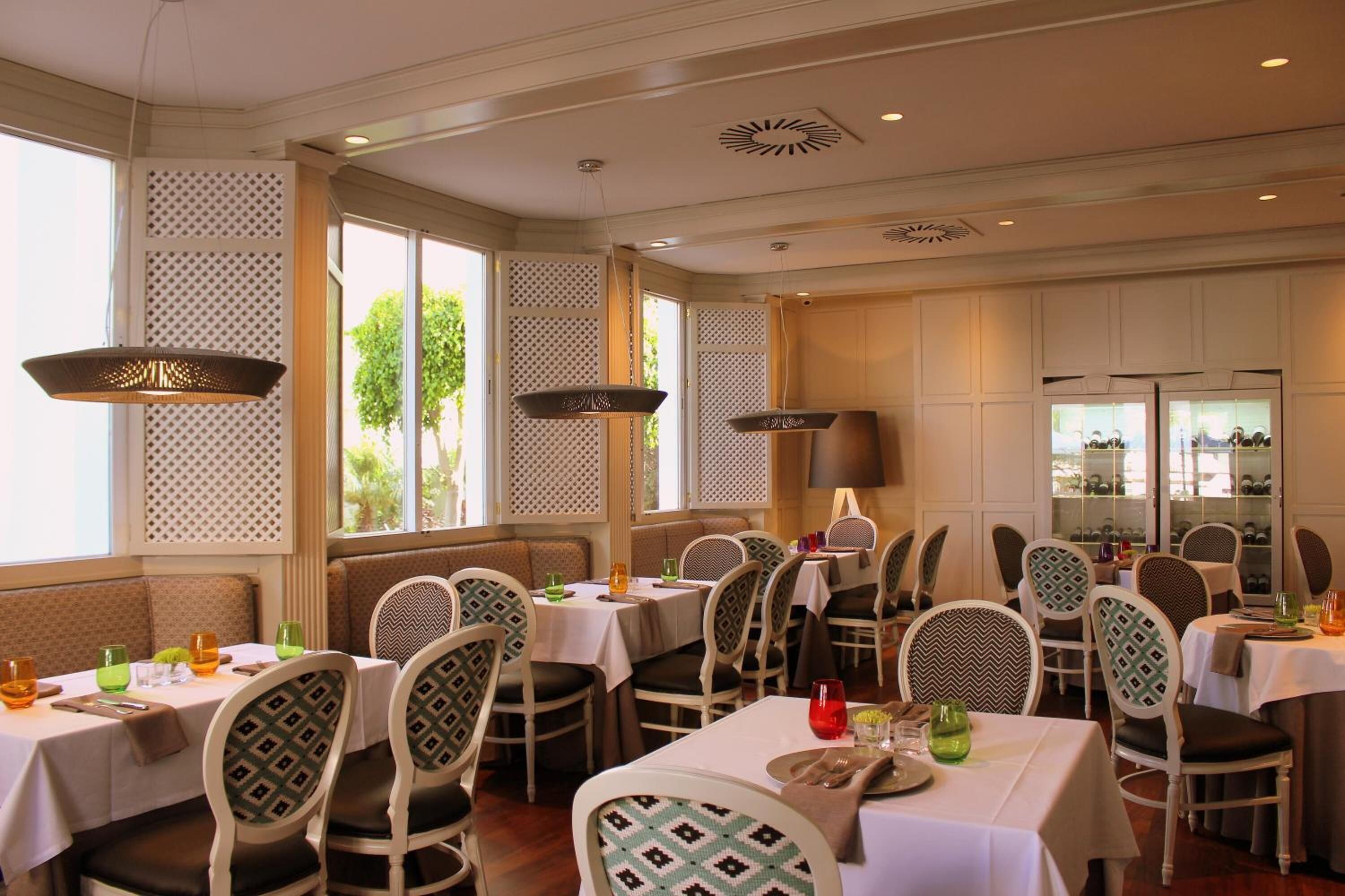 A dining area with tables and chairs, large windows, and decorative lighting fixtures.