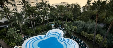 A swimming pool with a wavy edge design, surrounded by palm trees and greenery.