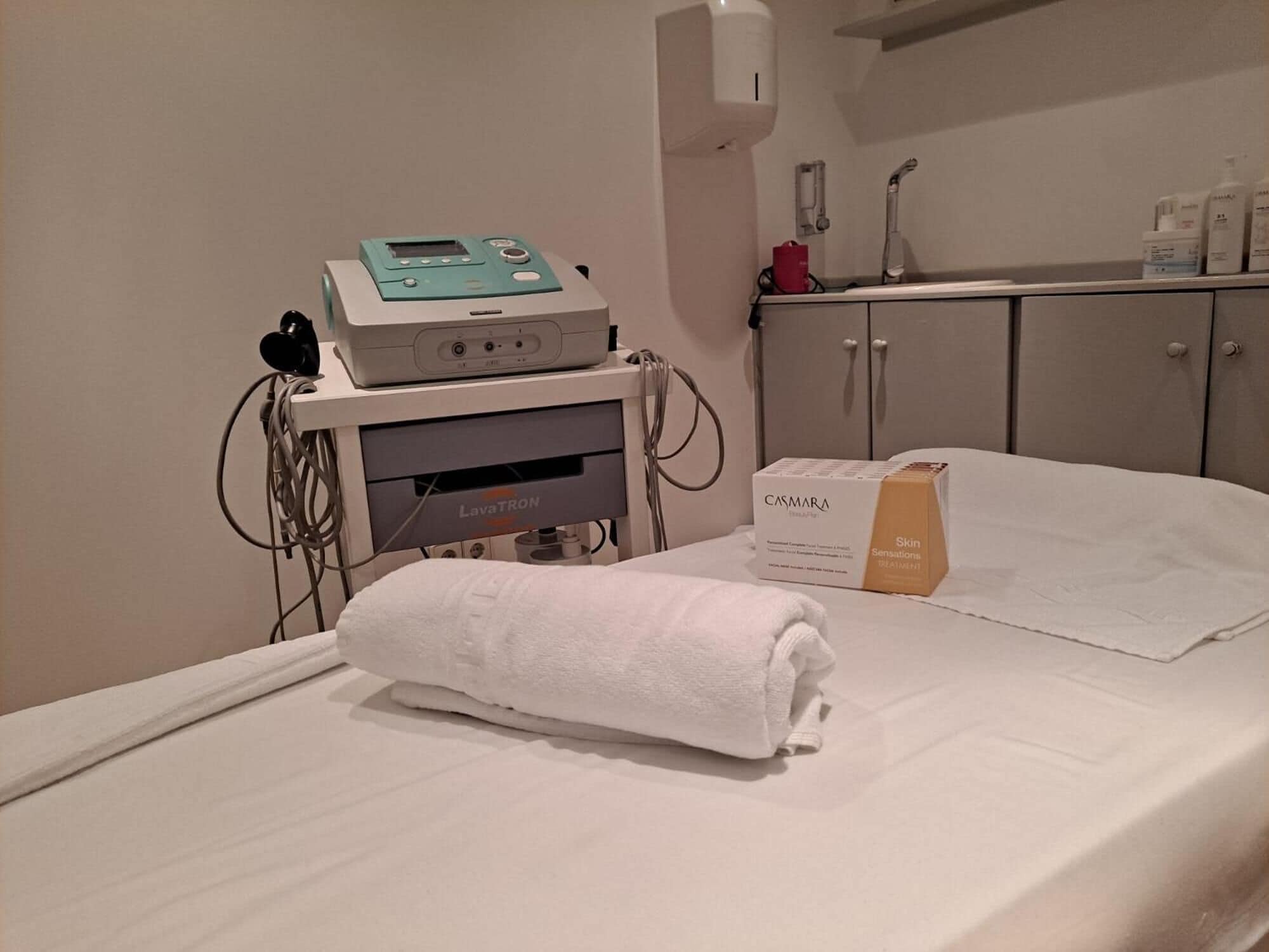 Una sala de tratamientos médicos con una cama, un equipo de tratamiento y un armario con botellas.