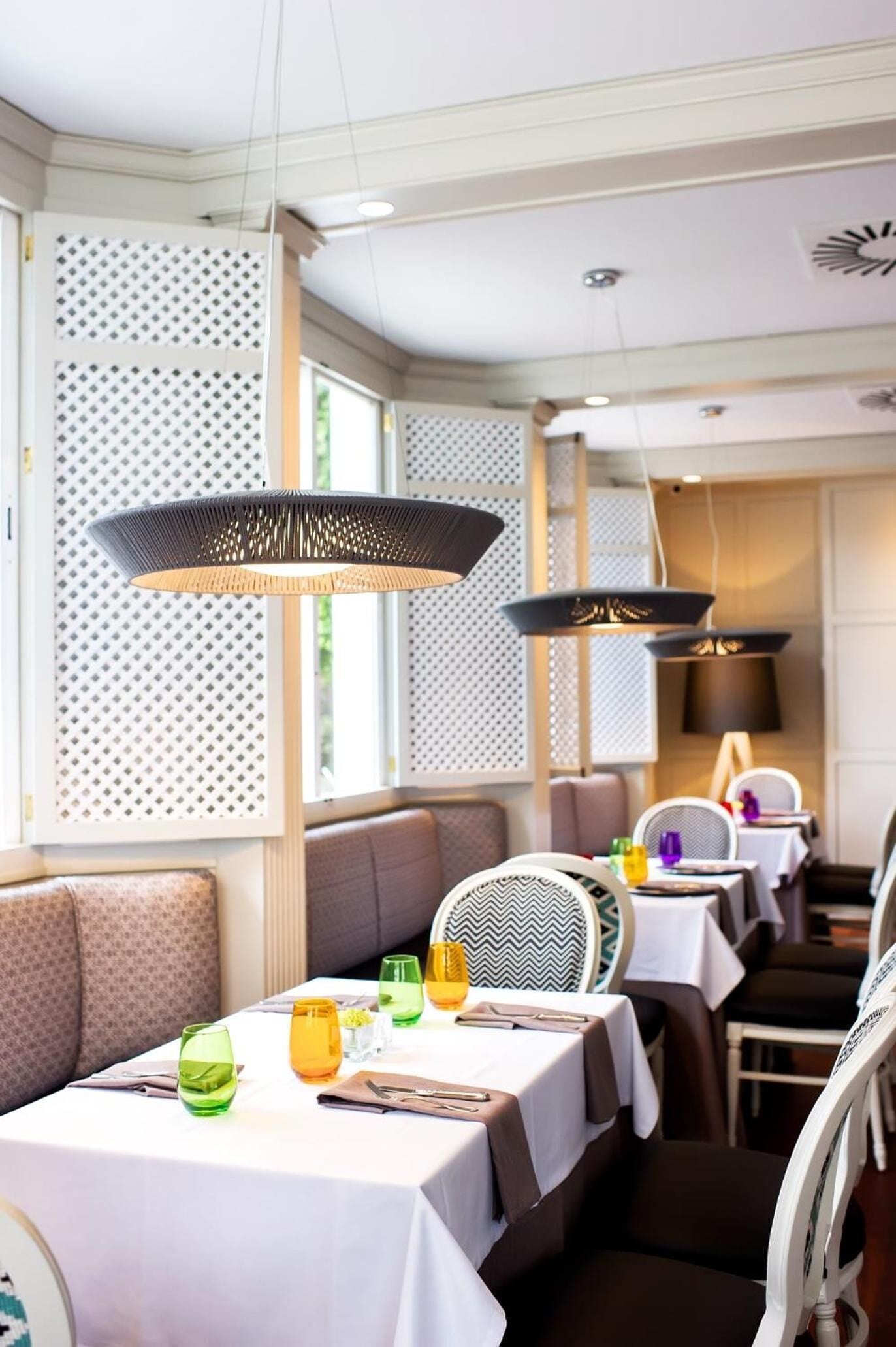 Un restaurante con cabinas y mesas, iluminación colgante y un separador decorado.