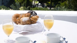 Preparación de desayuno con pastelería y zumo de naranja en un balcón con vistas a una ciudad con zonas verdes y edificios.