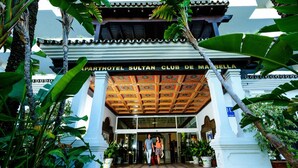 La entrada del Parthotel Sultan Club de Marbella, con suelo de baldosas y plantas tropicales alrededor.
