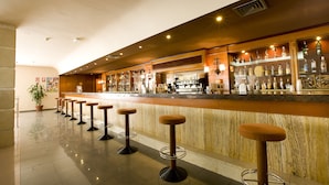 A bar area with a long counter, multiple stools, and a variety of bottles and glasses. - Hotel Monarque Fuengirola Park (Fuengirola)