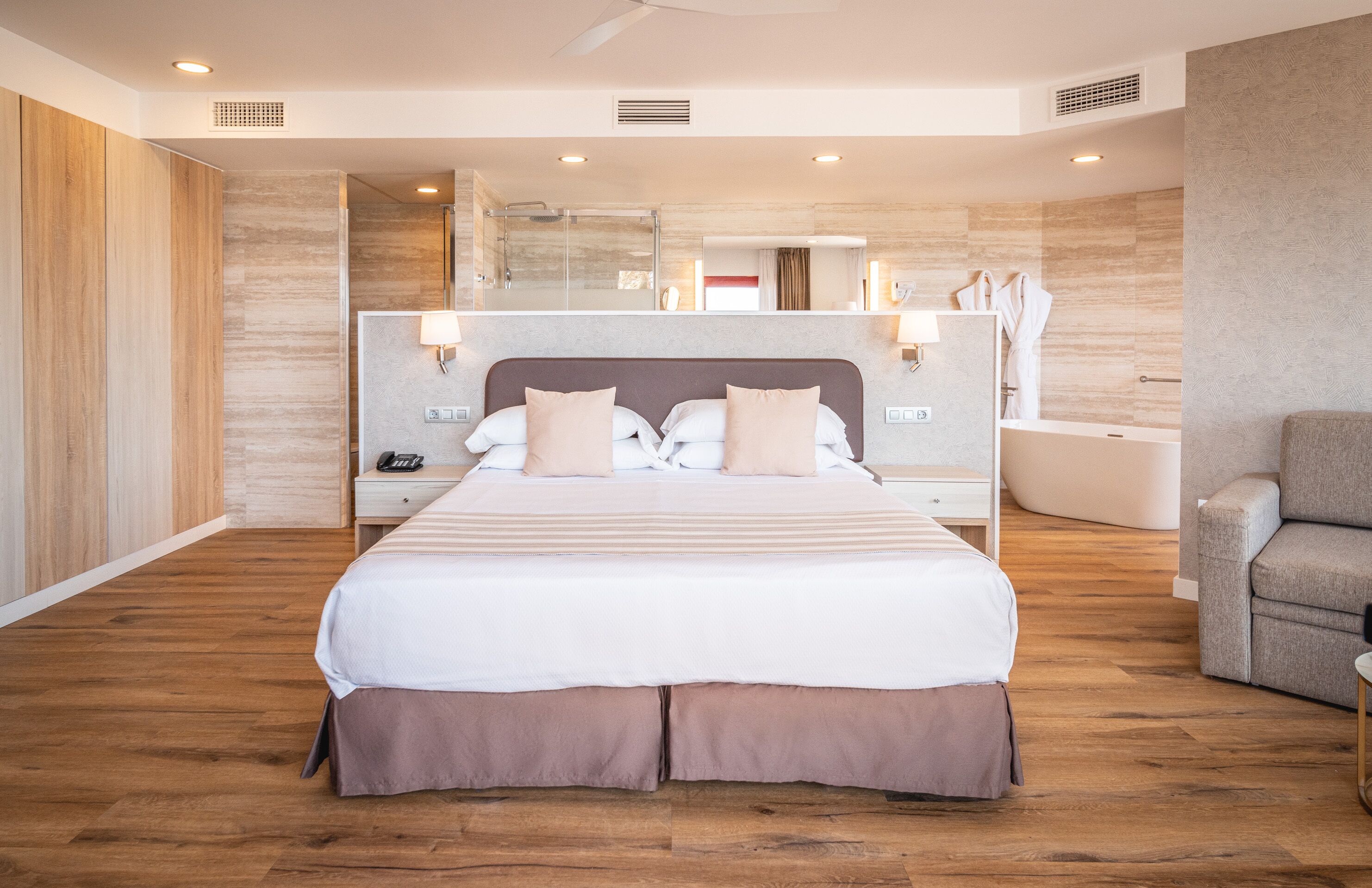 Ein modernes Hotelzimmer mit einem großen Bett, einer Sitzecke, einer Dusche und einem Schminktisch.