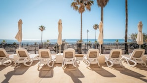 A beachside lounge with white rocking chairs and beige umbrellas, overlooking the sea. - Hotel Angela - Adults Recommended (Fuengirola)