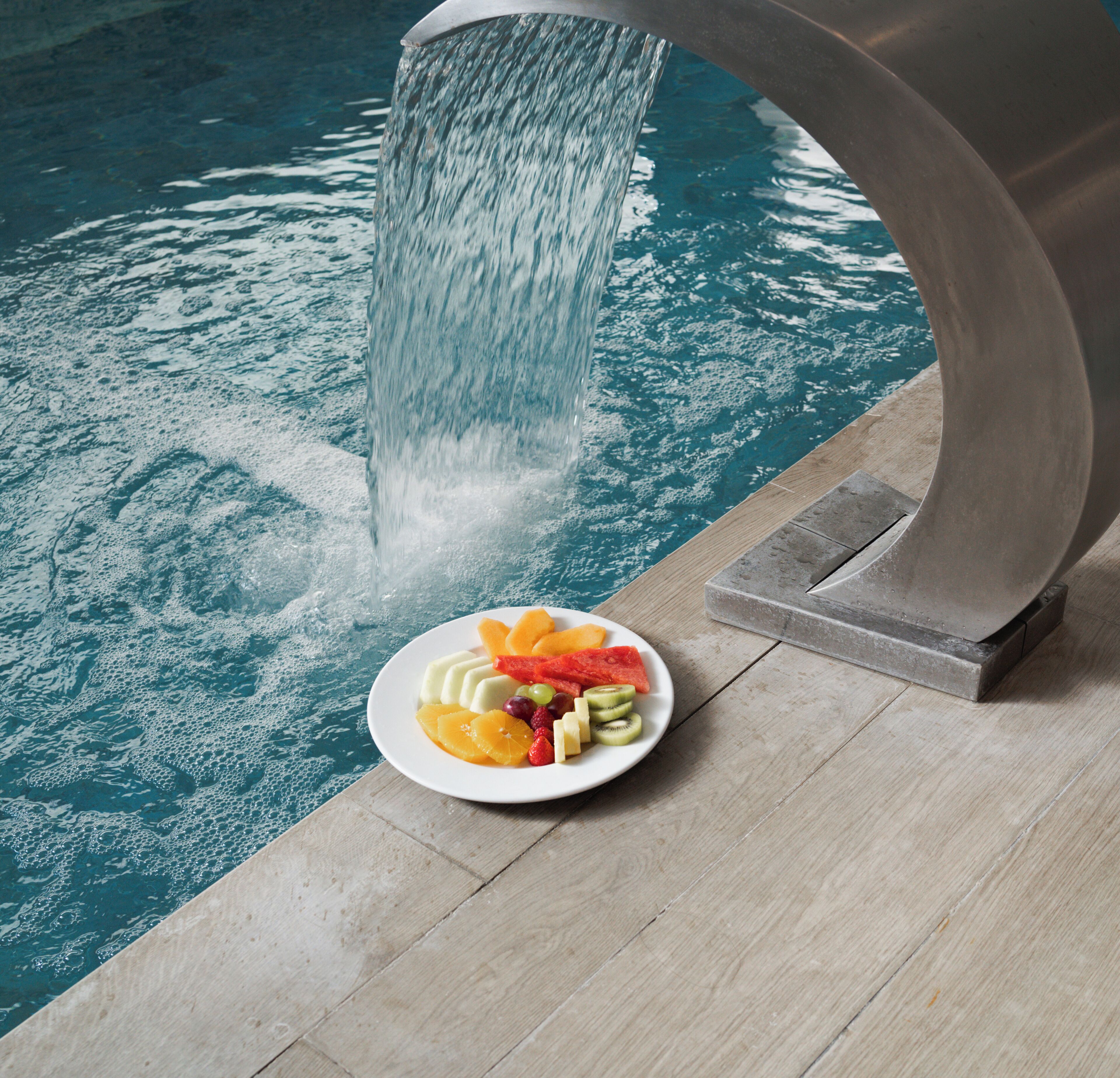 A poolside area with a plate of fruit and a water feature.