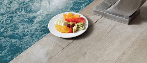 A poolside area with a plate of fruit and a water feature.