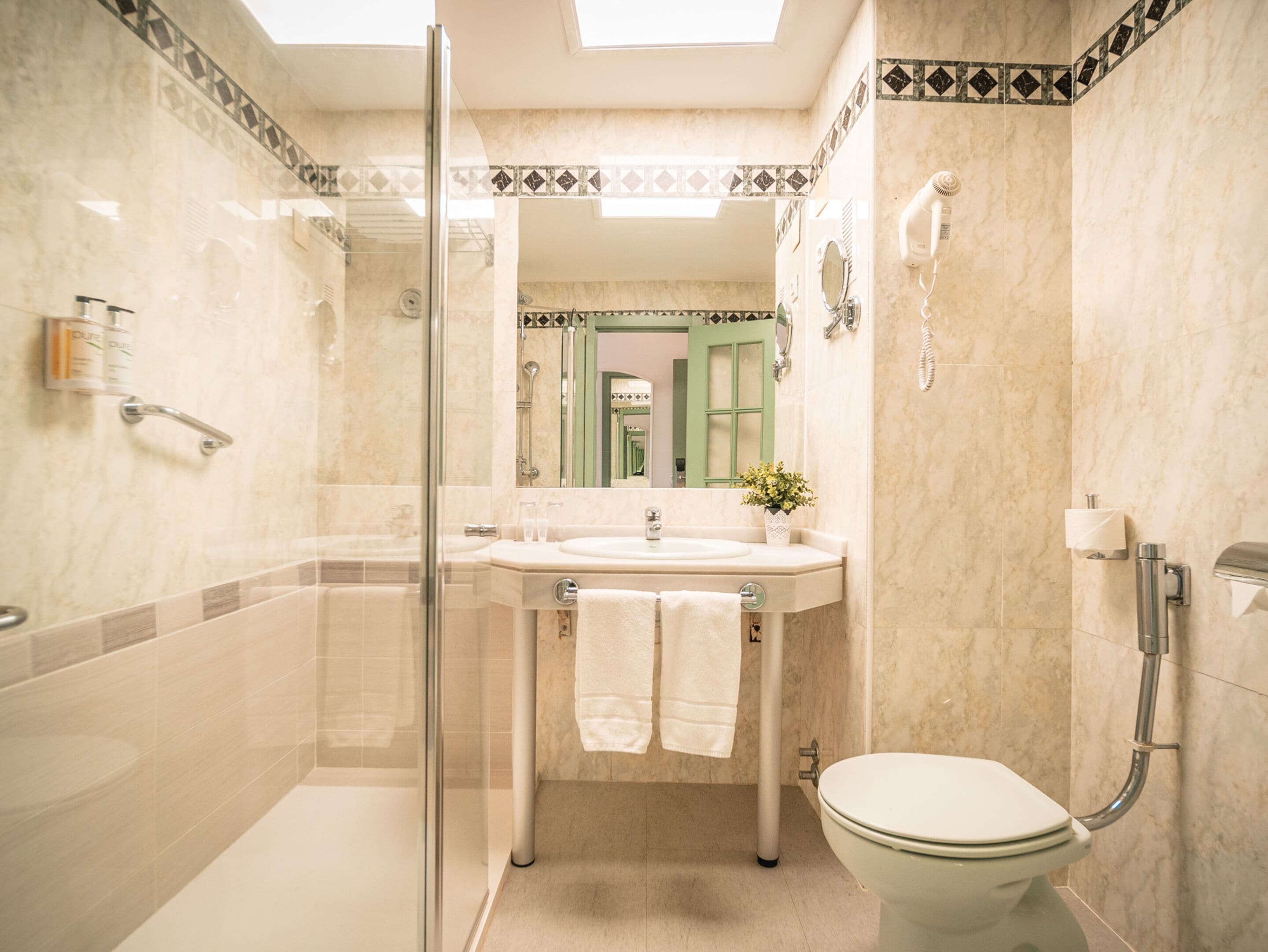 A bathroom with a glass shower enclosure, a sink with a mirror, a toilet, and a hand dryer.