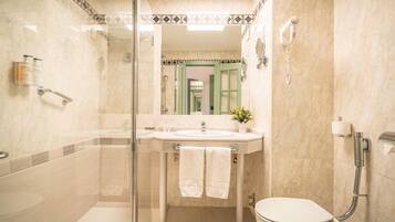 A bathroom with a glass shower enclosure, a sink with a mirror, a toilet, and a hand dryer.