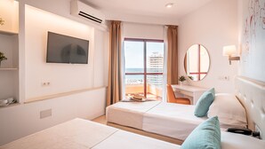 Habitación de hotel con dos camas, televisión, escritorio, silla, balcón con vista a un edificio y un espejo grande.