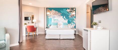 Una habitación de hotel moderna con una cama grande, un escritorio, una silla, un televisor y un mural decorativo en la pared.