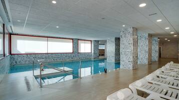 Una piscina con pared de azulejos y una ventana. Hay sillas de descanso y suelo de baldosas.