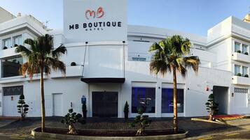 Ein modernes MB Boutique Hotel mit einem gut sichtbaren MB-Logo, heller Fassade und Palmen im Vordergrund.