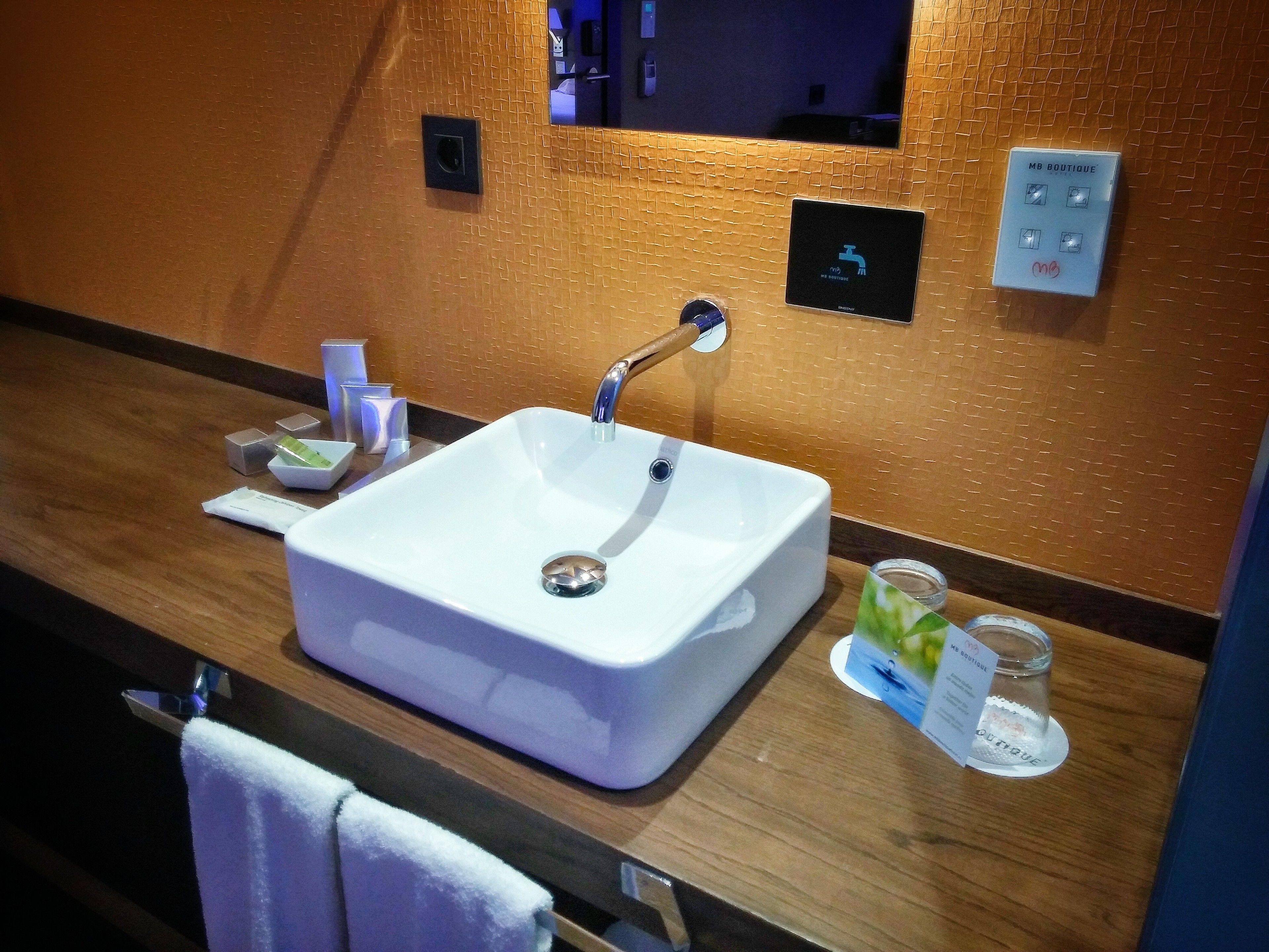 Un bany amb un lavabo blanc, un mirall, un suport per tovalloles i una petita estant amb productes de tocador.