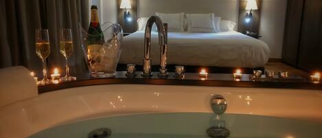 A hotel room with a large bathtub, a bed with white linens, and two bedside lamps.